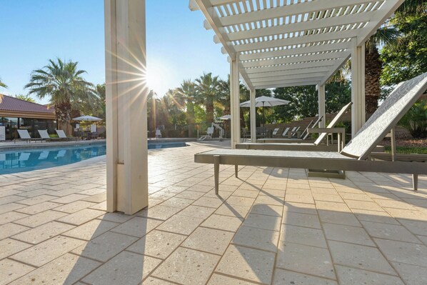 Zona junto a la piscina con sillones de descanso, una pérgola y vista despejada a la piscina.