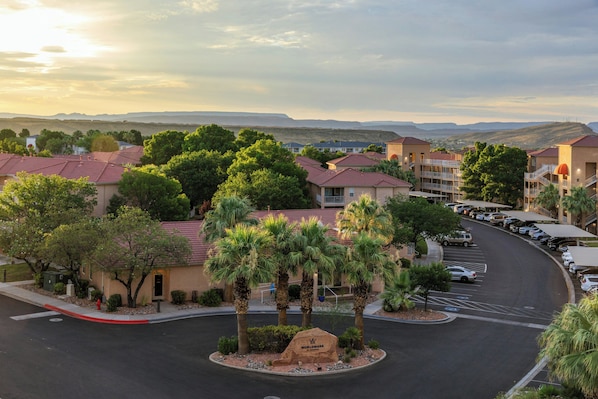 A residential area with multiple-story buildings, a parking lot, and a clear view of distant hills.