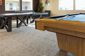 A pool table in a room with a carpeted floor, a dark wooden table, and a chair.