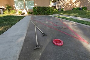 A paved area with two brooms and a red circular object, likely a mop bucket, in the center.