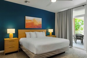 Habitación de hotel con una cama grande, dos mesitas de noche con lámparas, un cuadro en la pared y vistas al exterior a través de una puerta corrediza.