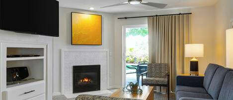 A modern living room with a flat-screen TV, a fireplace, a ceiling fan, and a view of the outdoors.
