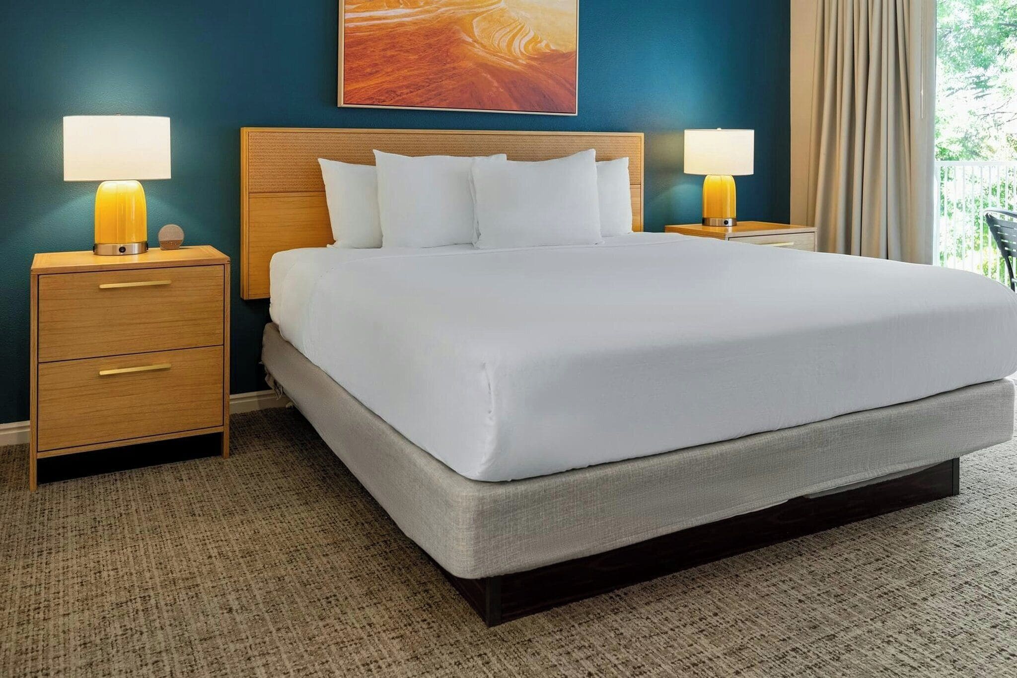 A hotel room with a large bed, two bedside tables with lamps, a headboard, and a painting on the wall.