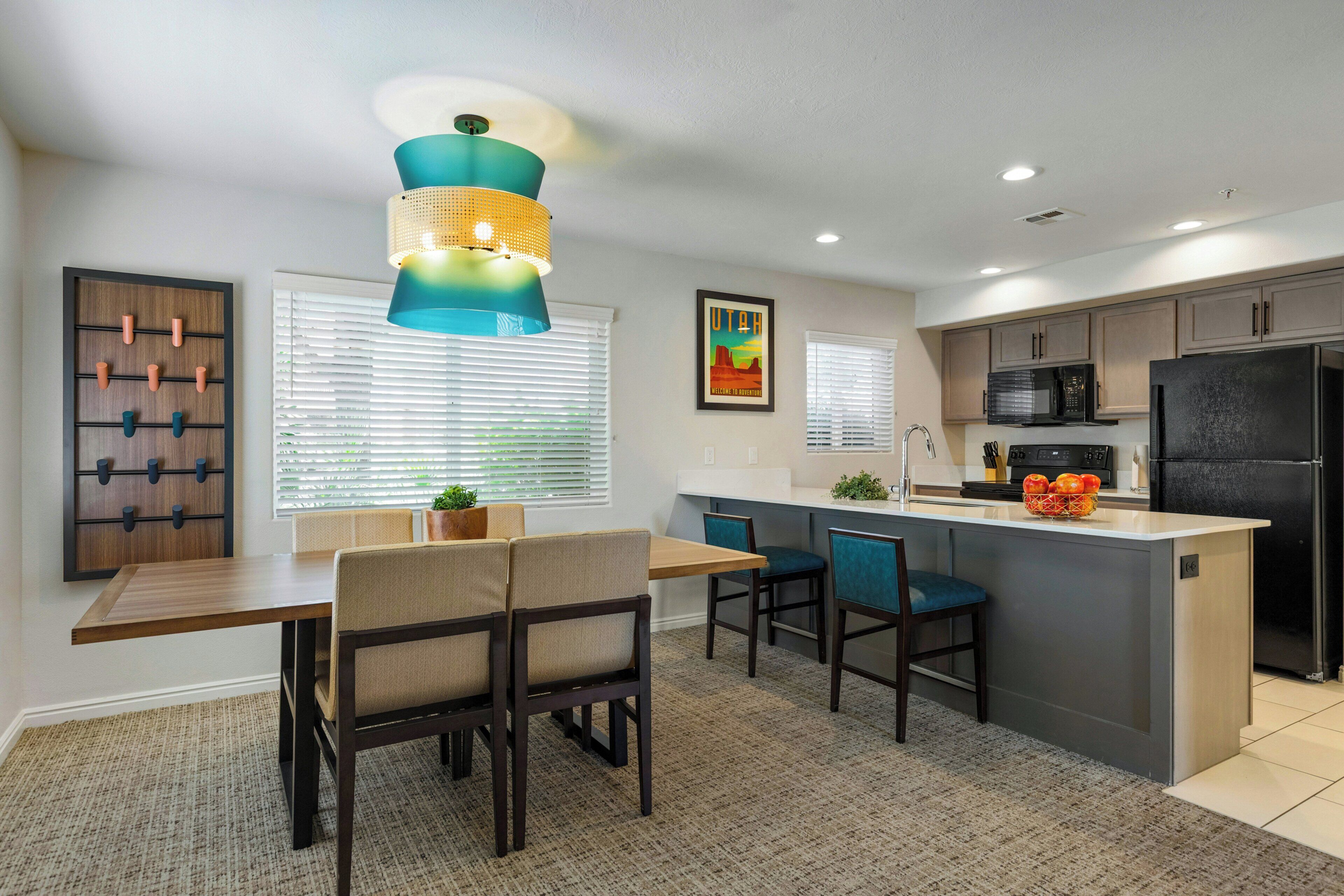 A modern kitchen with a central island, a dining area with chairs, and a wall-mounted rack.