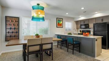 A modern kitchen with a central island, a dining area with chairs, and a wall-mounted rack.