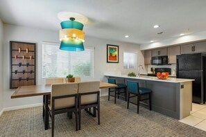 Una cocina moderna con una isla central, una zona de comedor con sillas y un estante en la pared.