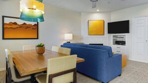 A modern living room with a wooden dining table, blue sofa, and a ceiling fan.