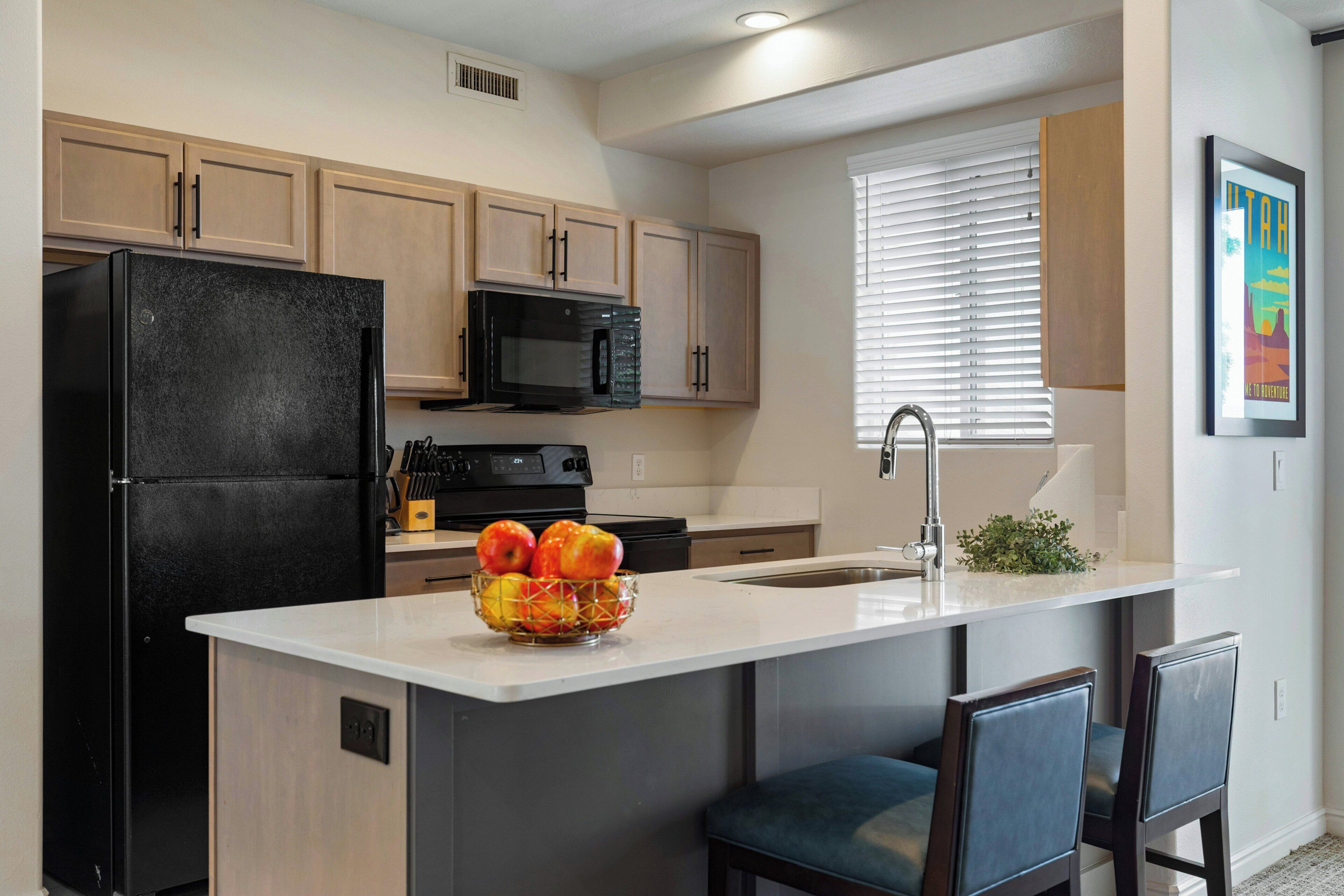 A modern kitchen with a black refrigerator, a microwave, and a sink with a faucet. There is a bowl of fruit on the counter.