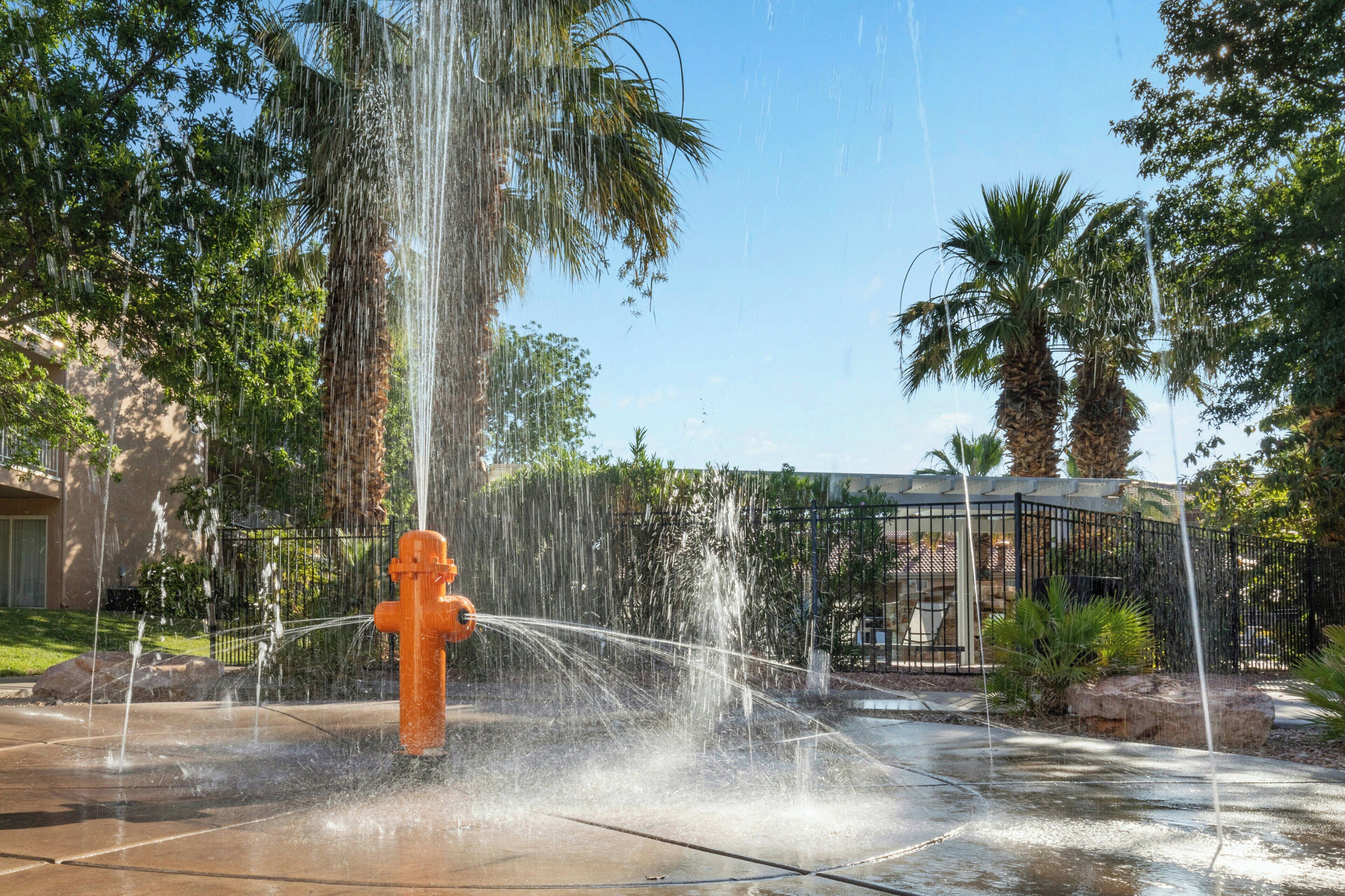 Un élément décoratif aquatique avec une structure centrale de couleur orange, entouré de palmiers et se dressant sous un ciel dégagé.