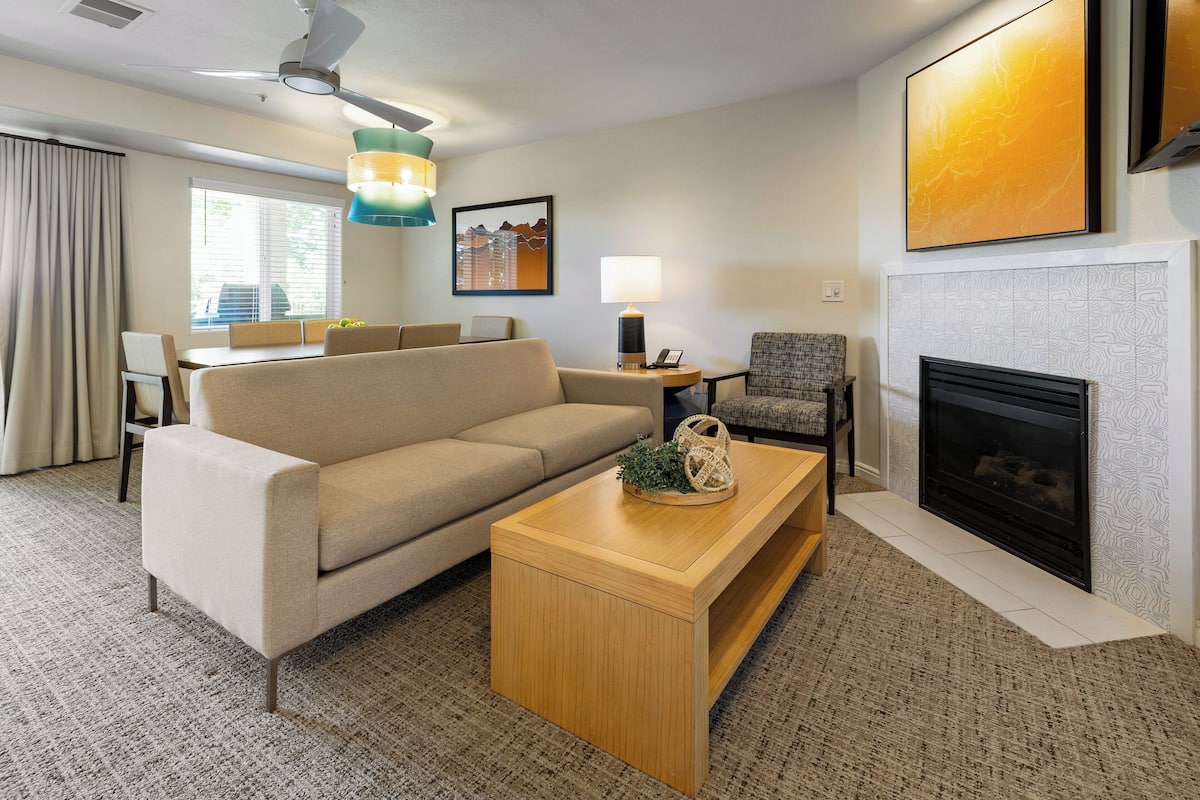 A modern living room with a sofa, coffee table, and fireplace. There is a dining area with a table and chairs.