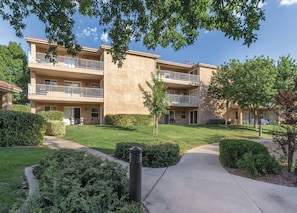 A multi-story residential building with balconies, a well-maintained lawn, and a clear sky.