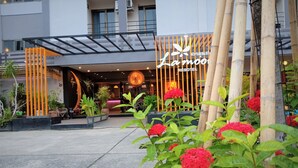 Una entrada de hotel moderna con mostrador de recepción, plantas de interior y una valla de bambú.