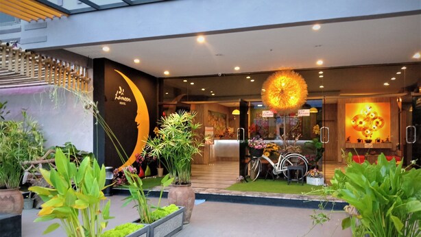 Entrada de hotel con diseño moderno, destacada por un gran mural de luna y sol, una bicicleta y plantas en macetas.