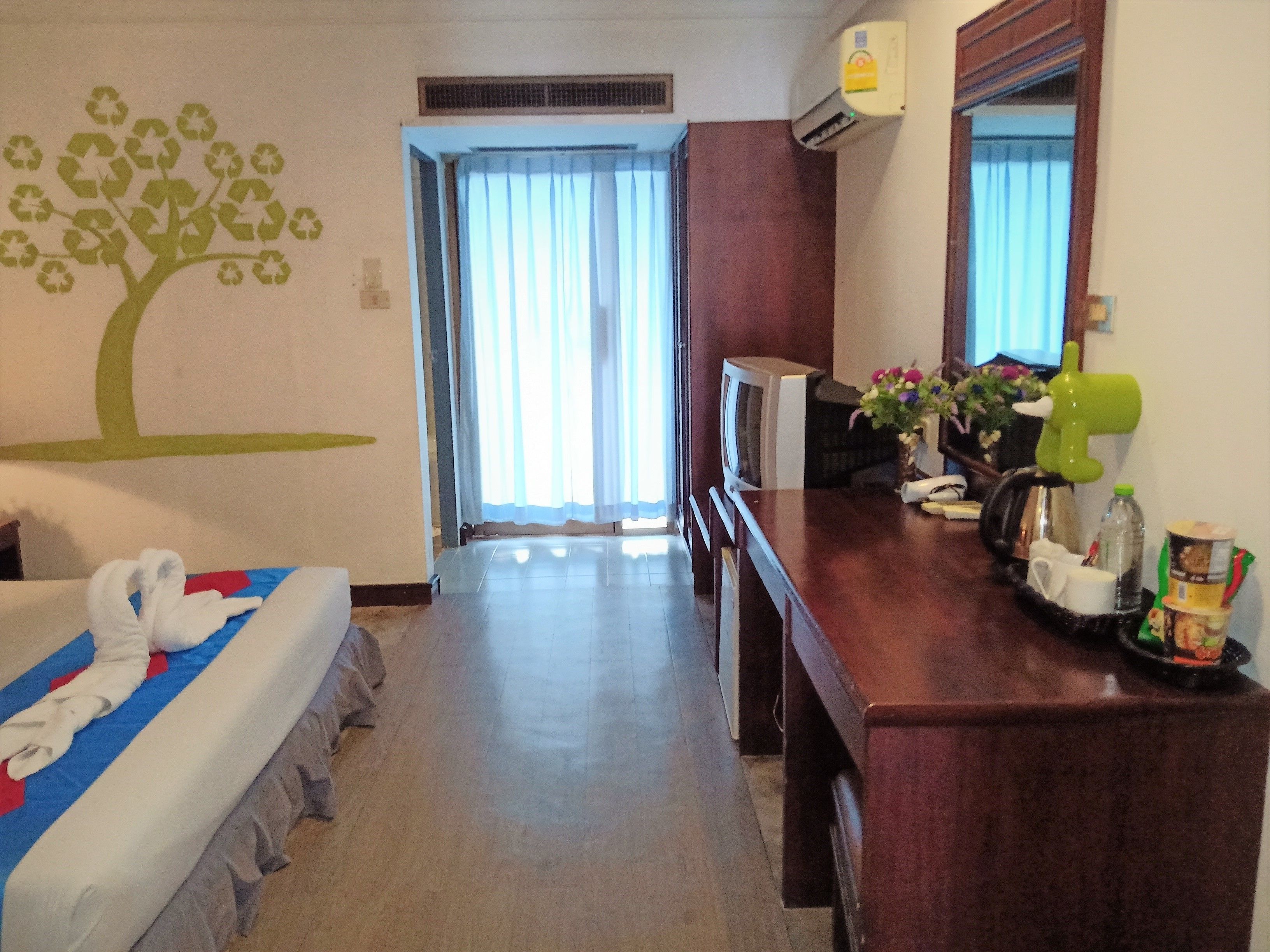 Una habitación de hotel con cama, escritorio, espejo y ventana con cortinas.