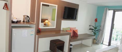 A hotel room with a bed, a desk with a mirror, a television, a refrigerator, and a small stool.