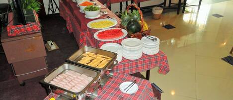 A buffet setup with various food items and utensils on tables covered with red and black checkered tablecloths.