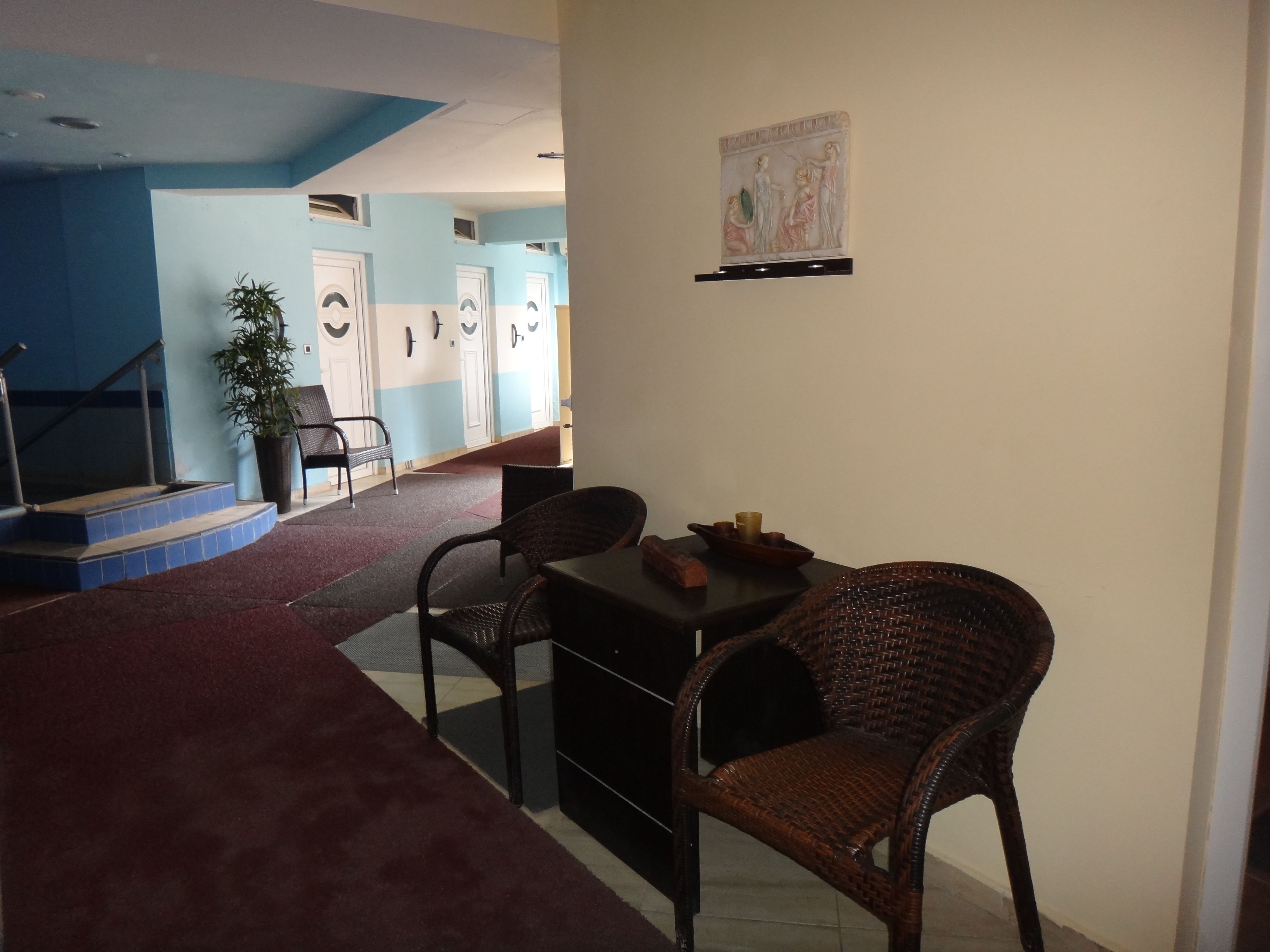 A lobby with a staircase, a reception desk, wicker chairs, a potted plant, and a wall-mounted artwork.