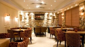 Restaurante com paredes de pedra, cadeiras estampadas e uma tela de televisão.
