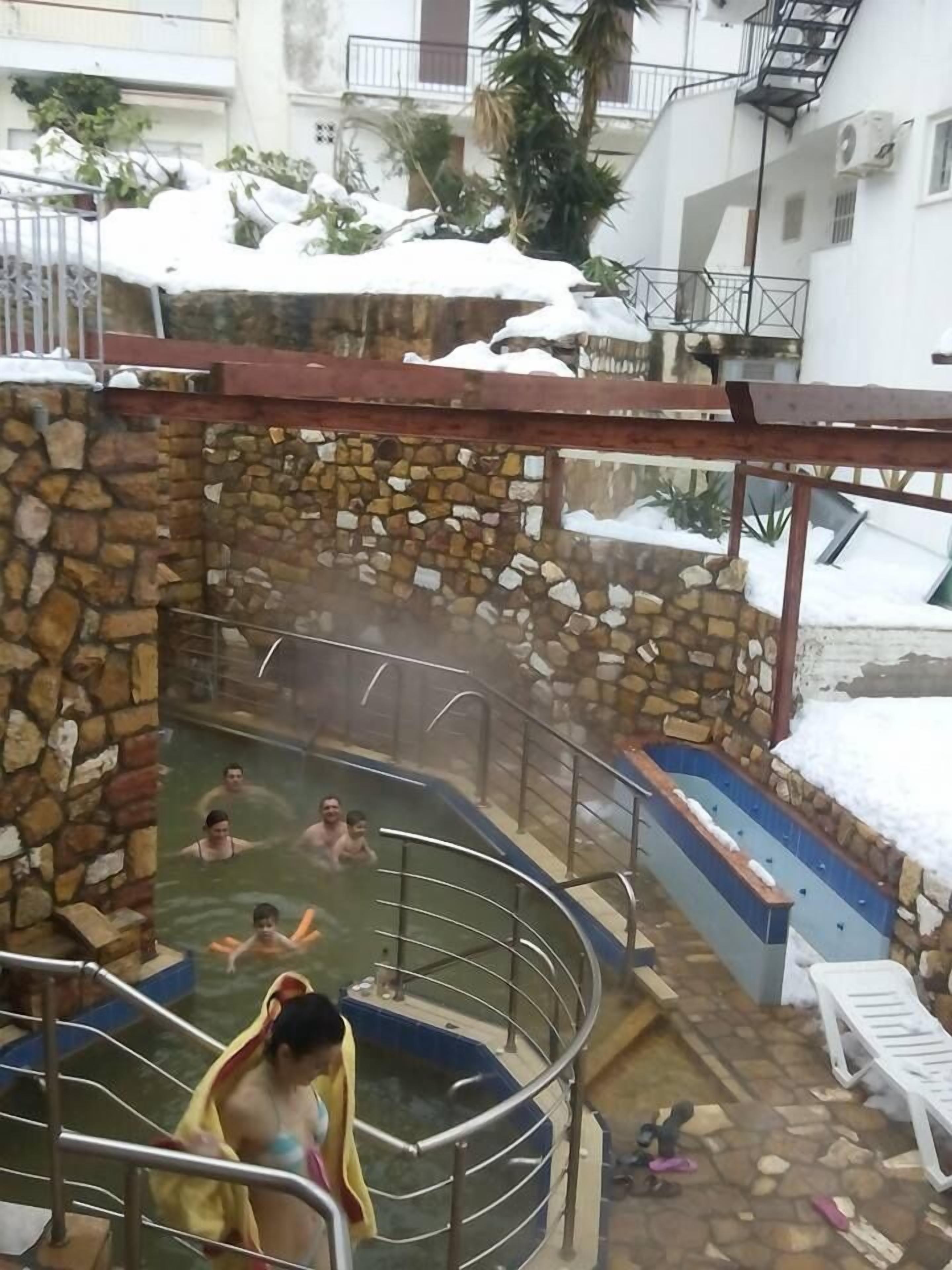 Zona de aguas termales con paredes de piedra, una piscina rodeada de nieve y edificios.