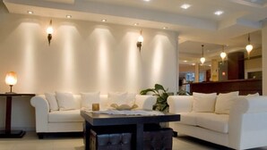 Sala de estar moderna com sofá branco, mesa de centro escura e iluminação embutida na parede.