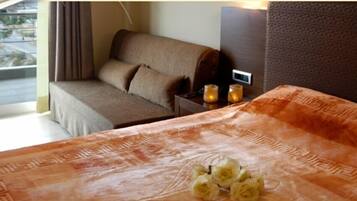 A hotel room with a bed, a sofa, a nightstand with a lamp, and a view of the outdoors.