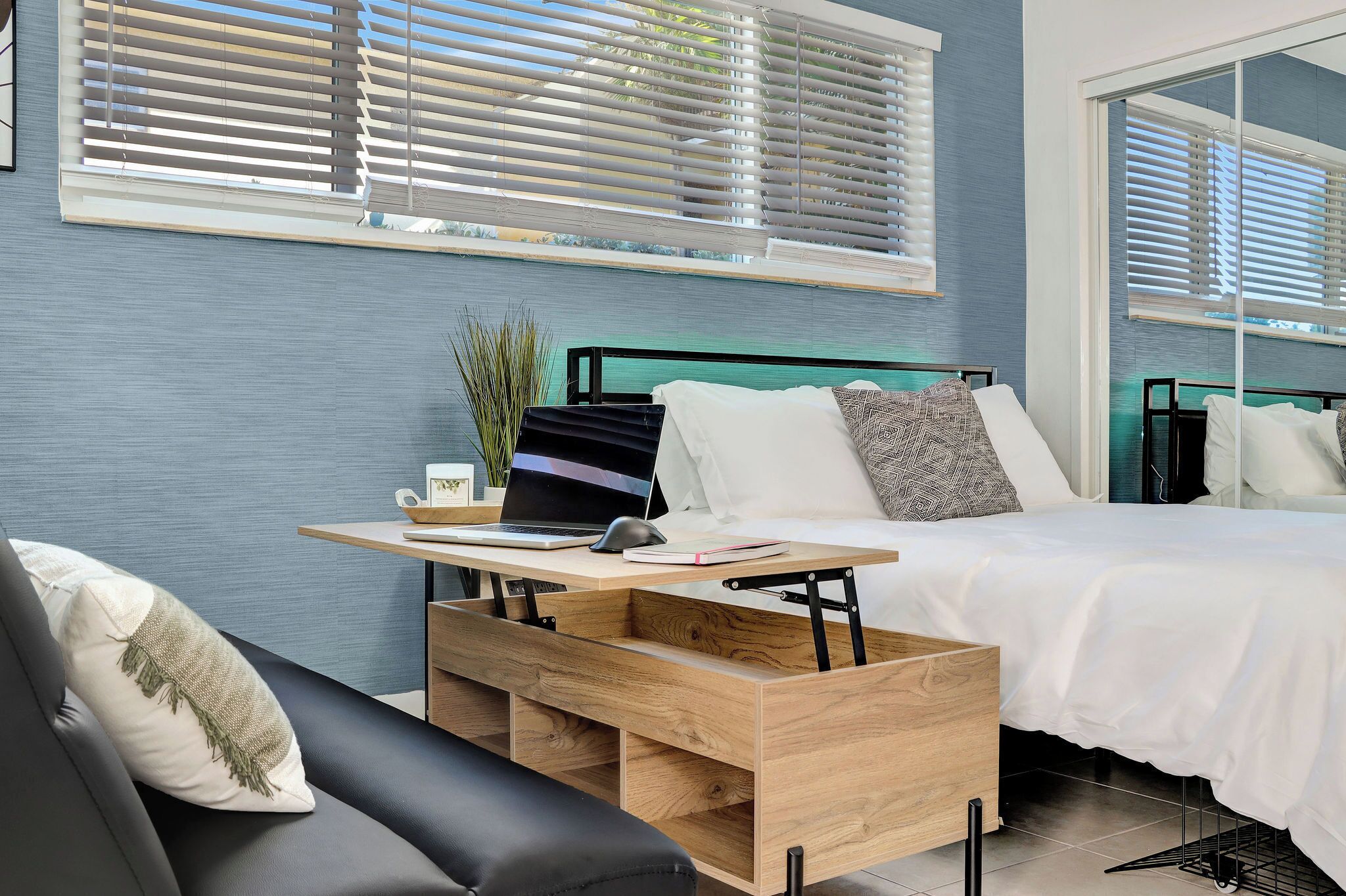 Une chambre moderne avec un lit, un bureau avec un ordinateur portable et une fenêtre équipée de stores.