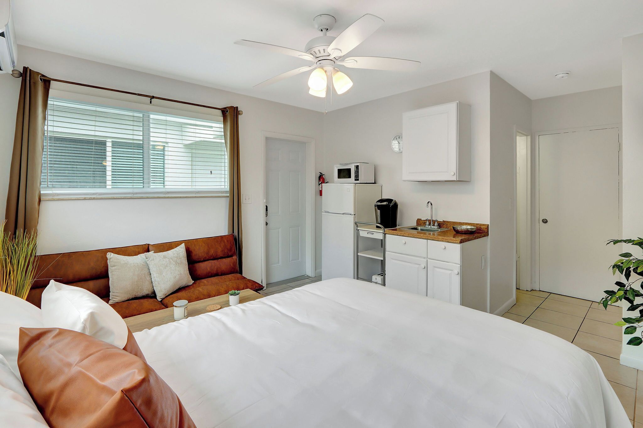 Una habitación de hotel con una cama, un sofá, una kitchenette y un ventilador de techo.