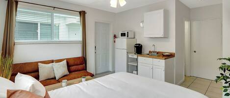 Una habitación de hotel con una cama, un sofá, una kitchenette y un ventilador de techo.