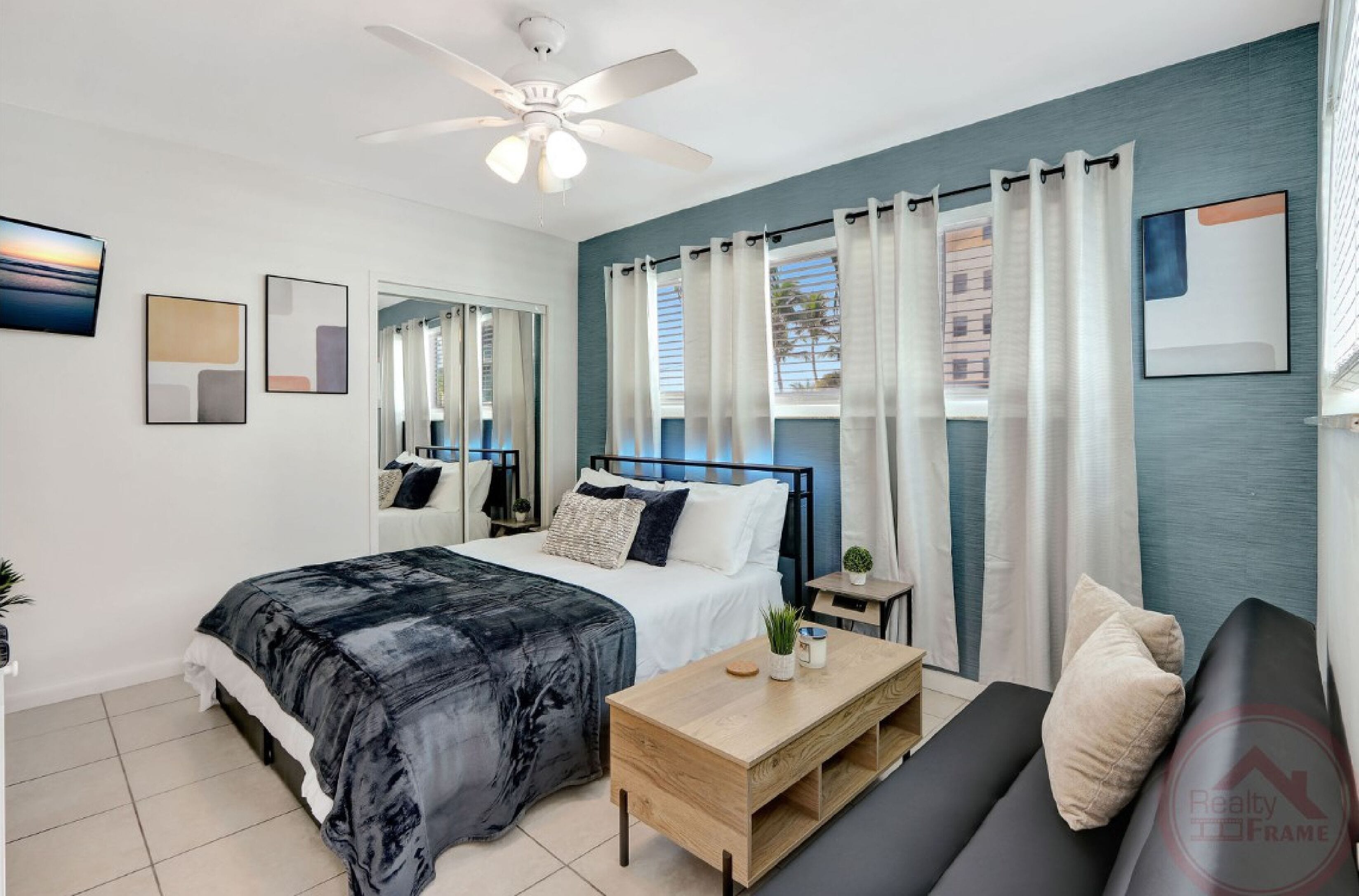A modern bedroom with a bed, a sofa, a coffee table, and a ceiling fan.