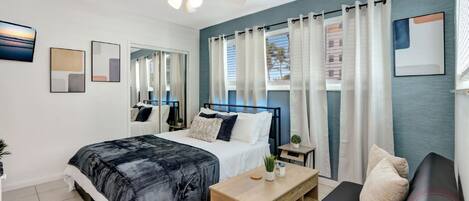 A modern bedroom with a bed, a sofa, a coffee table, and a ceiling fan.