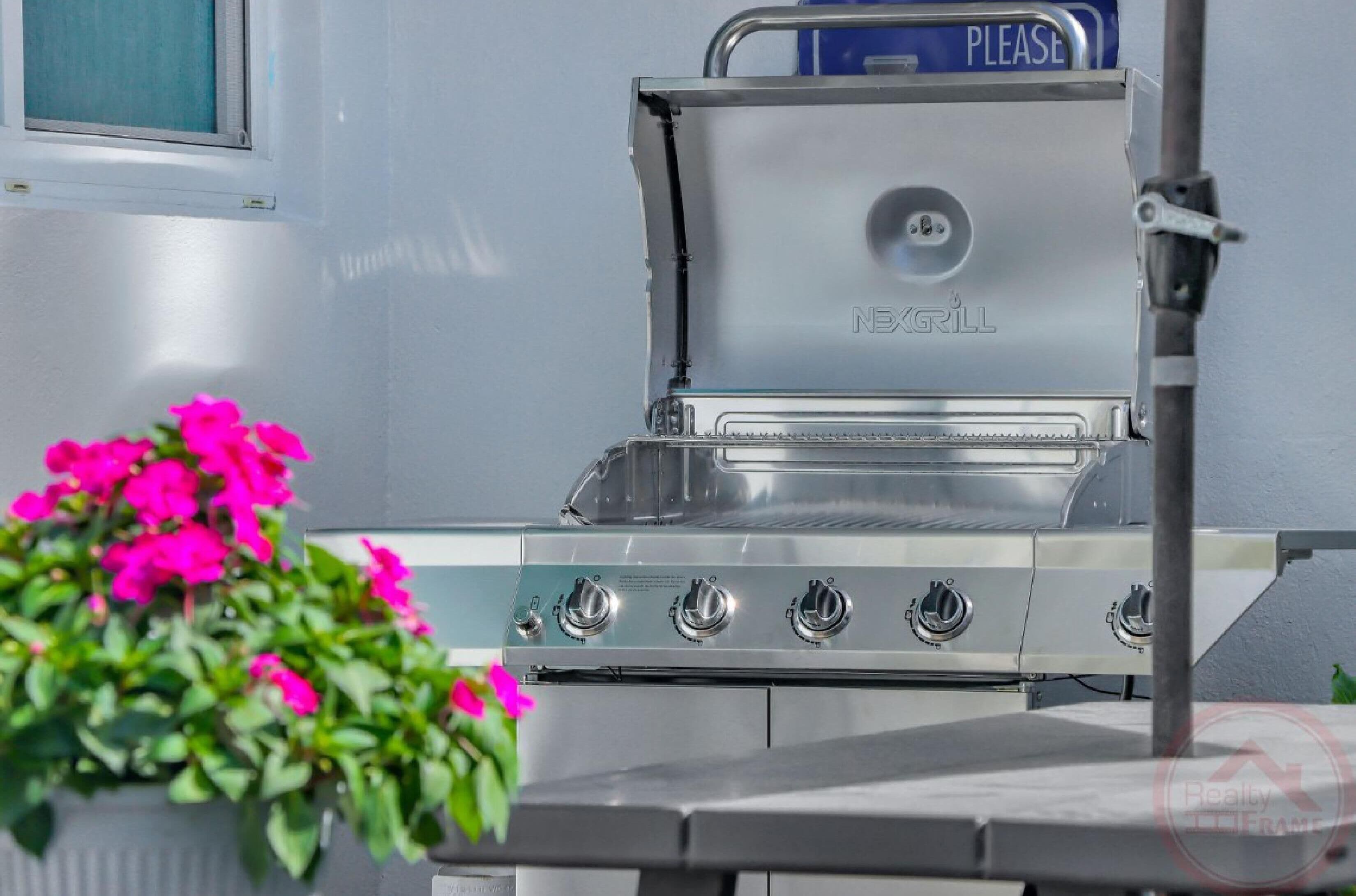 A stainless steel grill with four burners and a blue 'PLEASE' sign on top.
