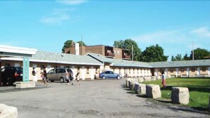 A building with a parking lot, a few cars, and people walking. - Parkway Motel (London)