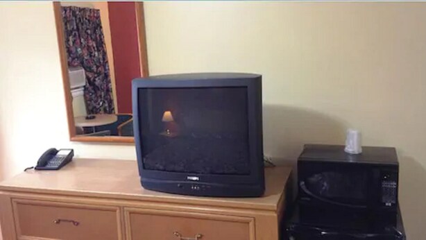 A television on a wooden dresser, a telephone, and a microwave. - Parkway Motel (London)