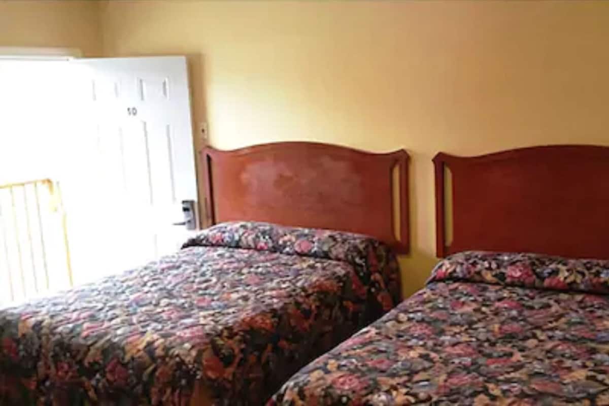 Two beds with floral bedding, wooden headboards, and a door with a number.