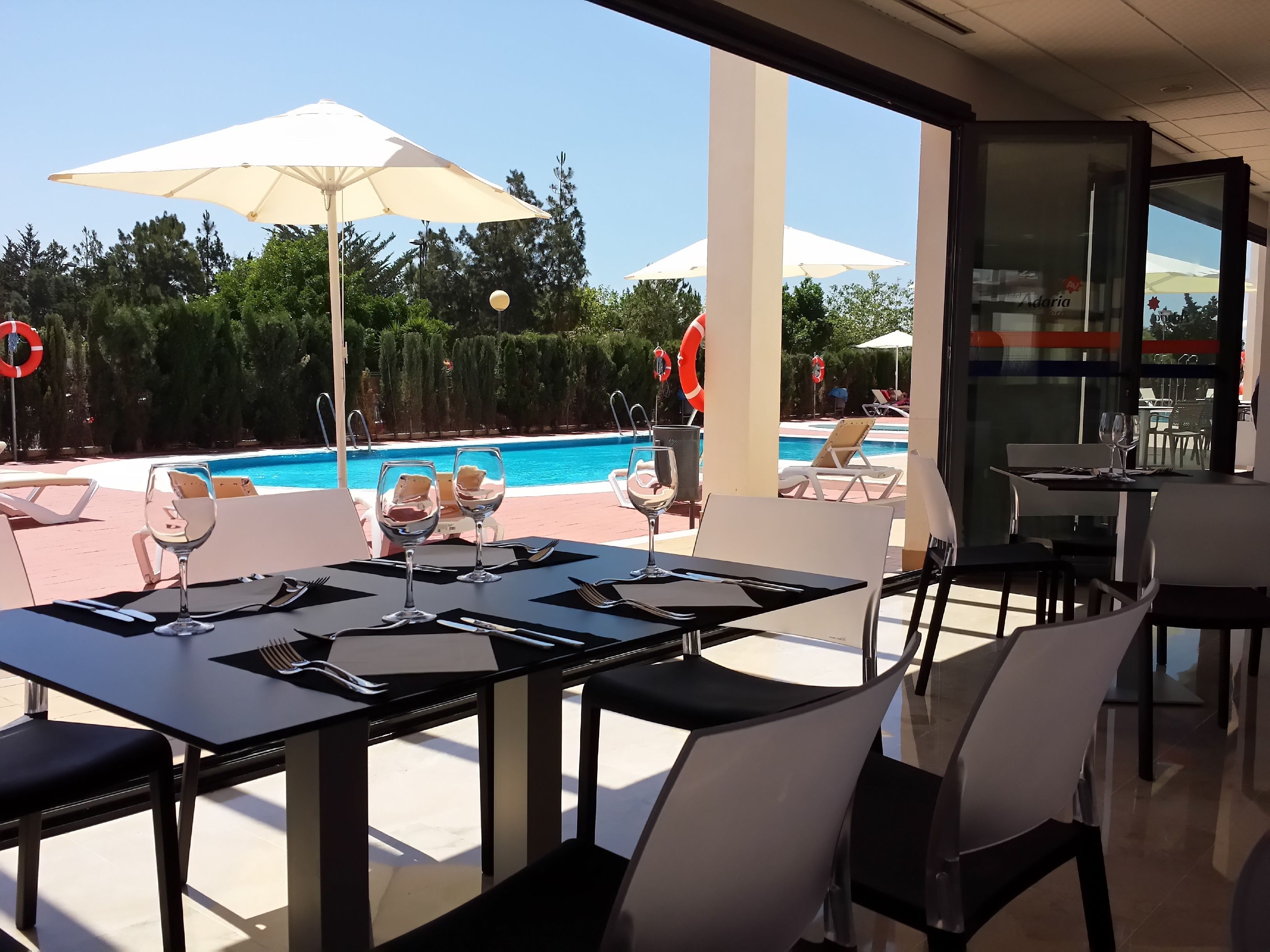 Un área de comedor al aire libre con mesas y sillas, con vistas a una piscina y sillones de descanso.