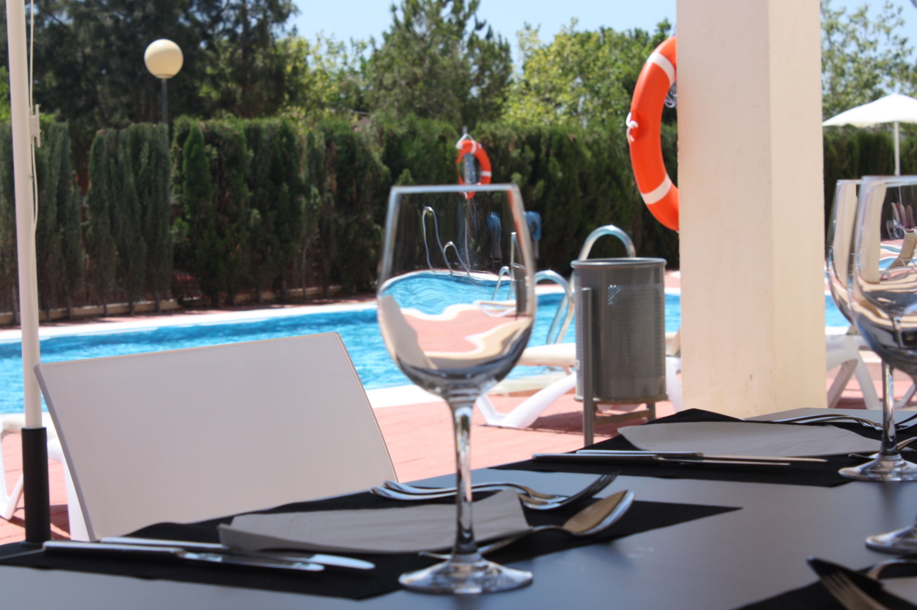 A dining table with a wine glass, a menu, and a laptop, overlooking a pool with lounge chairs and a life preserver.