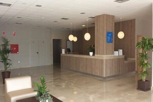 Uma área de recepção com um balcão de madeira, duas luminárias pendentes e plantas em vasos.