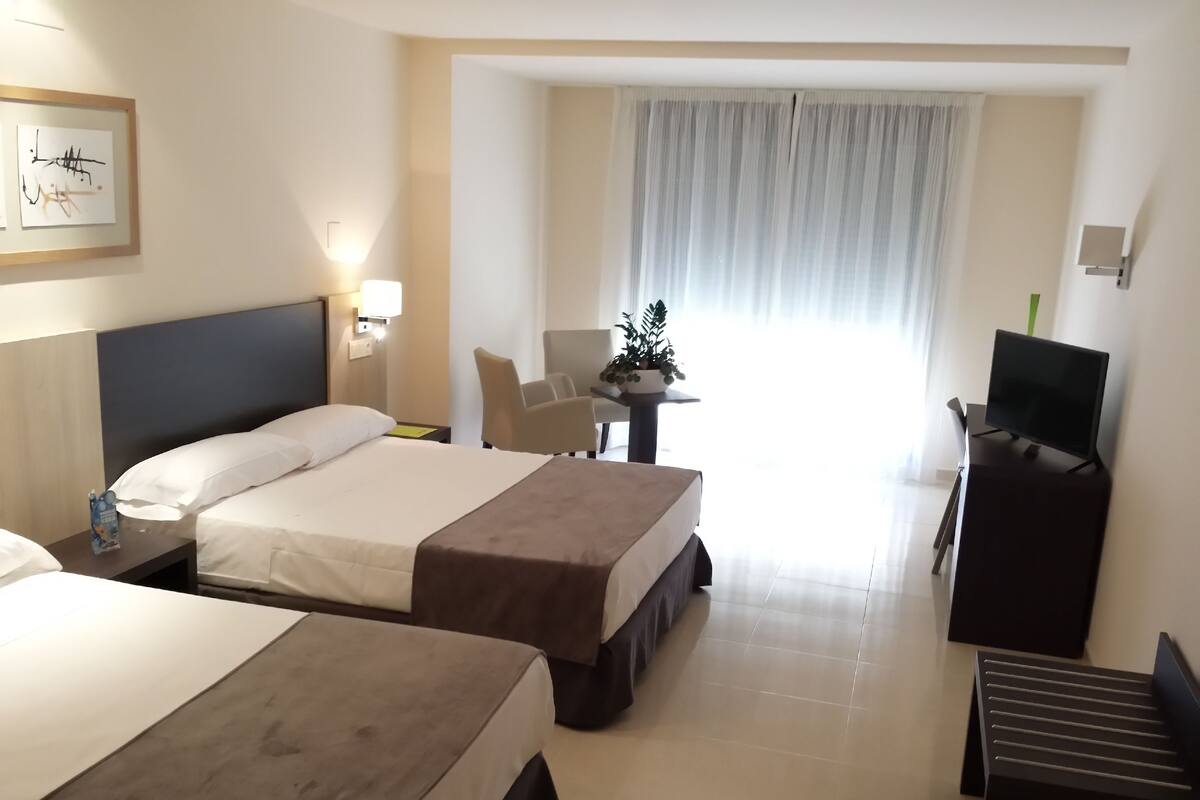 A hotel room with two beds, a desk, a TV, and a window with curtains.