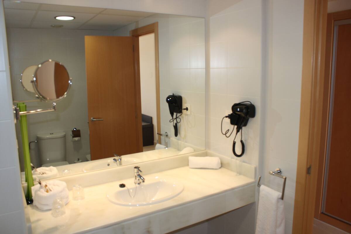 A hotel bathroom with a large mirror, a sink, a towel rack, and a hairdryer.