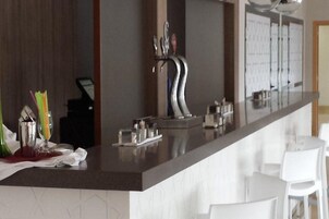 Una cocina moderna con barra, sillas blancas y un lavamanos de acero inoxidable.
