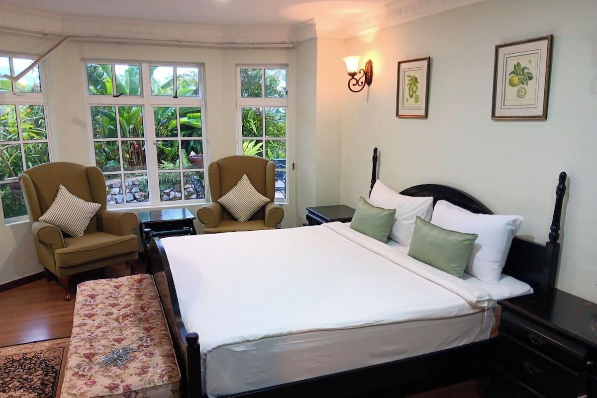 A bedroom with a large bed, two armchairs, a bench, and a nightstand.