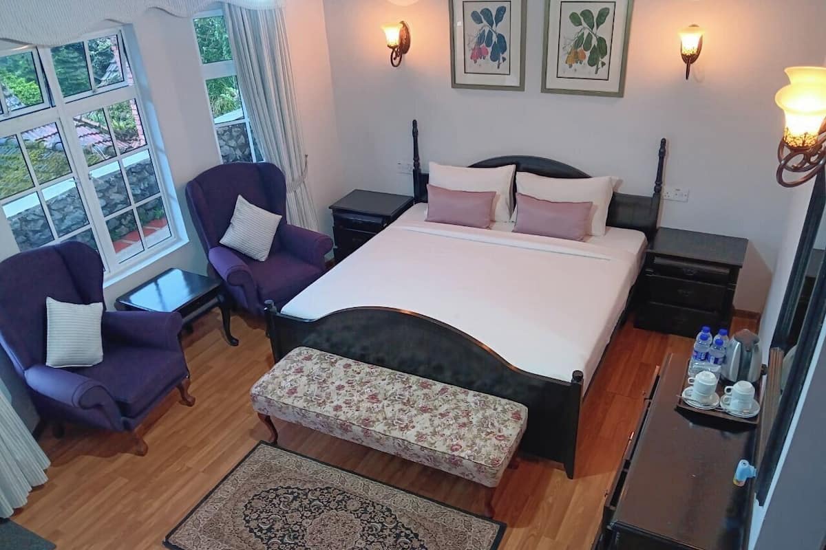 A bedroom with a bed, two chairs, a bench, a nightstand, a table, and a window with curtains.