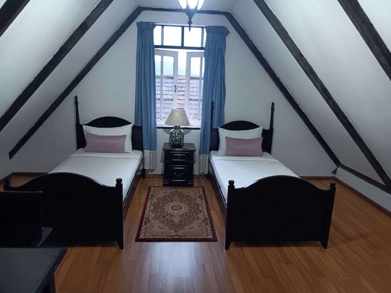 Un dormitorio con dos camas, una mesita de noche, una lámpara y una ventana con cortinas.