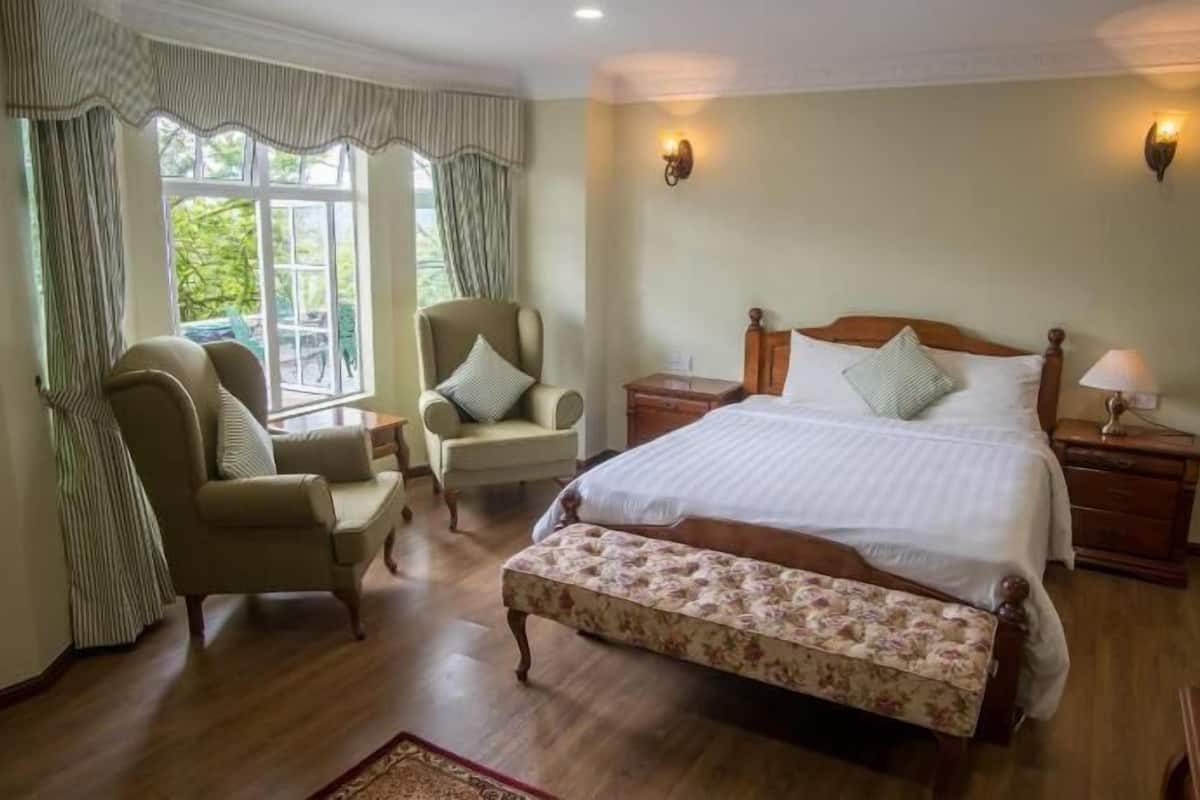 A bedroom with a bed, two chairs, a bench, a nightstand, and a window with curtains.