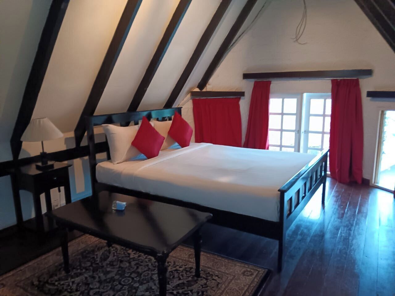 Una camera da letto con un letto, un comodino, un tavolo e una finestra con tende rosse.