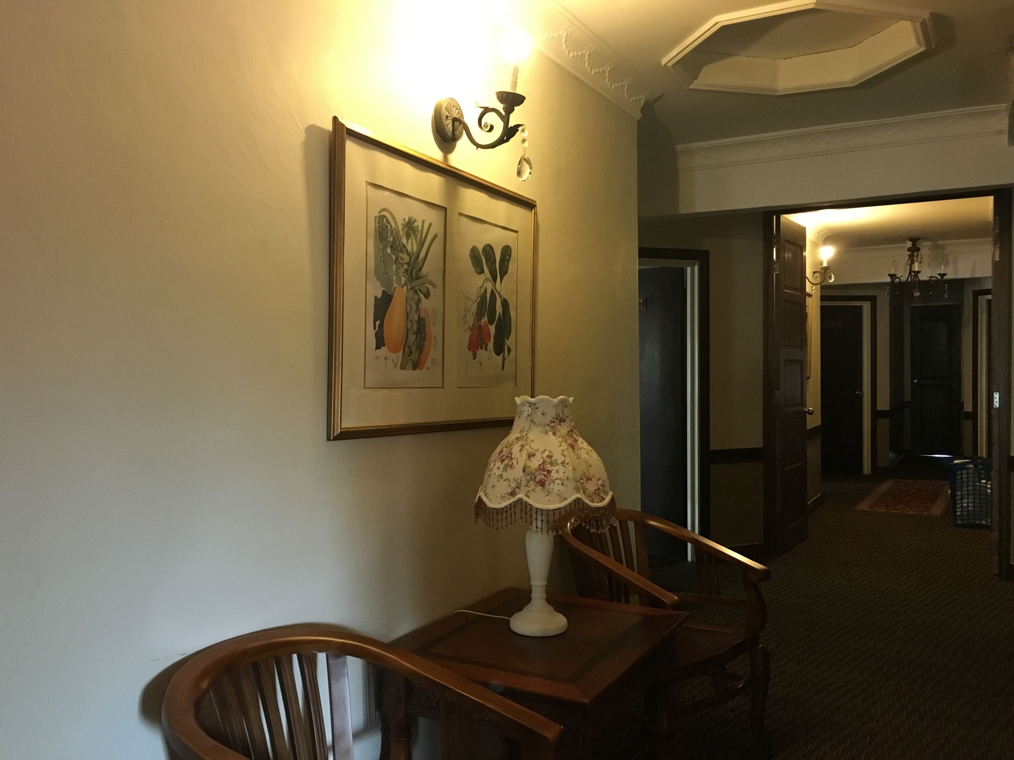 Un pasillo con una mesa y sillas de madera, una lámpara de pared y reproducciones botánicas enmarcadas.