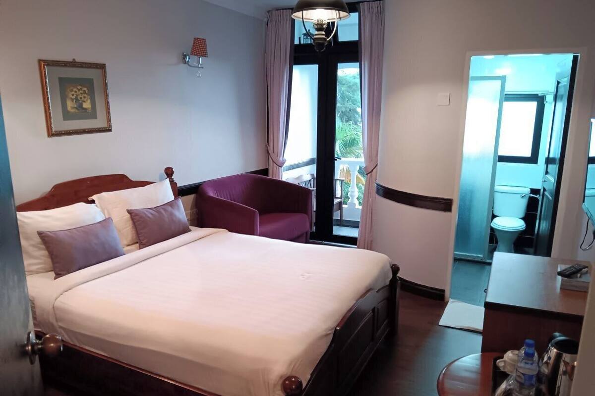 A hotel room with a large bed, a desk, a chair, and a view of the outdoors through a glass door.