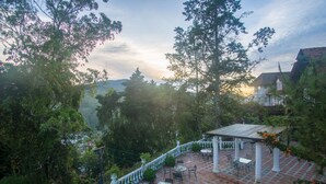 A patio with outdoor seating, surrounded by lush greenery and a view of distant hills. - The Bala's Holiday Chalet (Tanah Rata)