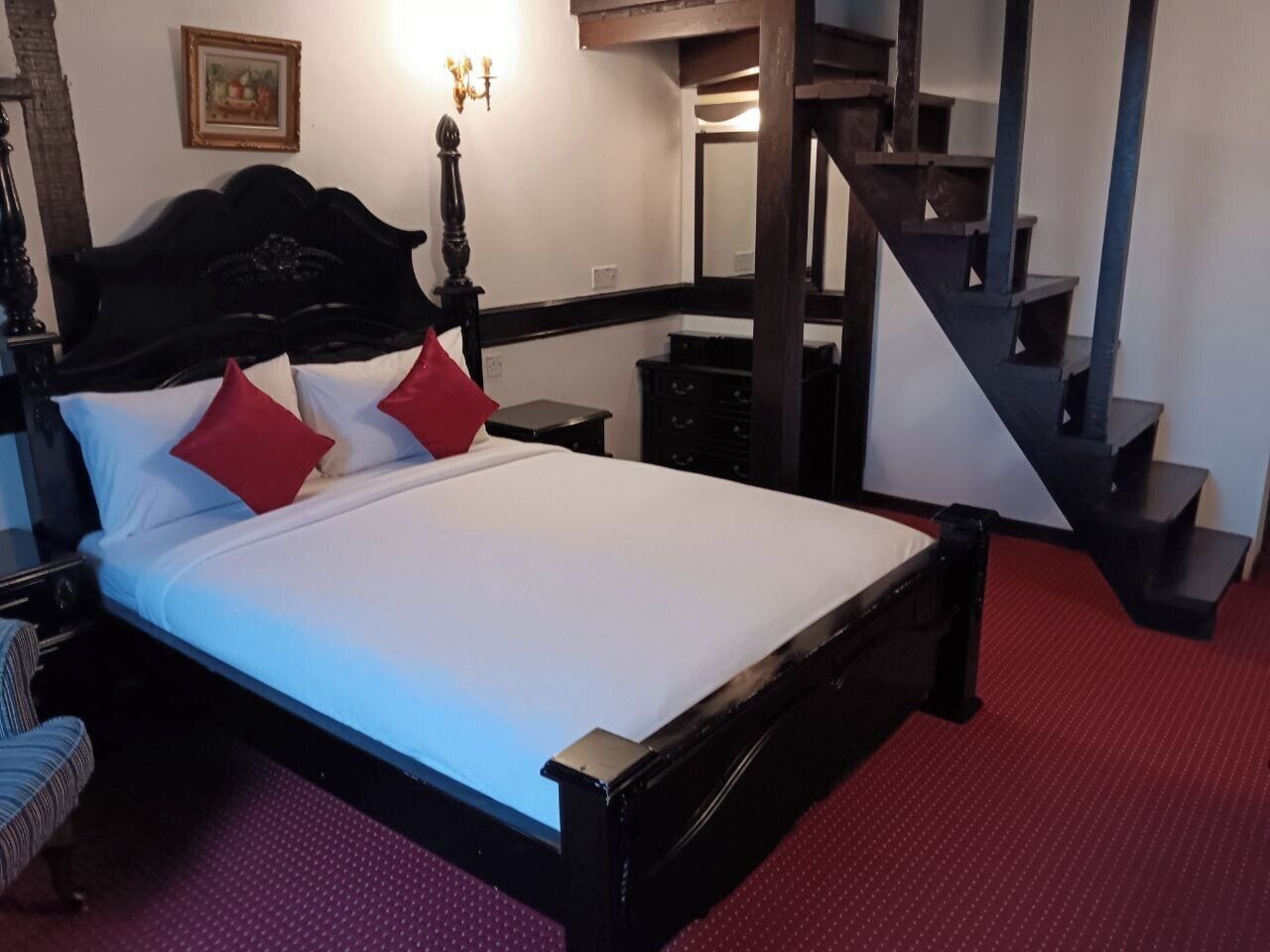 Une chambre à coucher avec un grand lit, une tête de lit en bois, une moquette rouge, un escalier et un tableau accroché au mur.