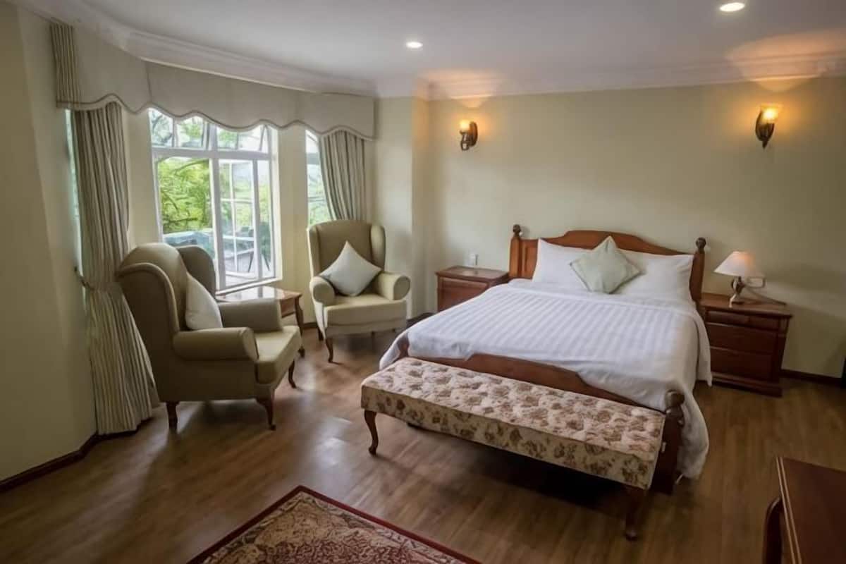 A bedroom with a large bed, two bedside tables, a chair, and a window with curtains.